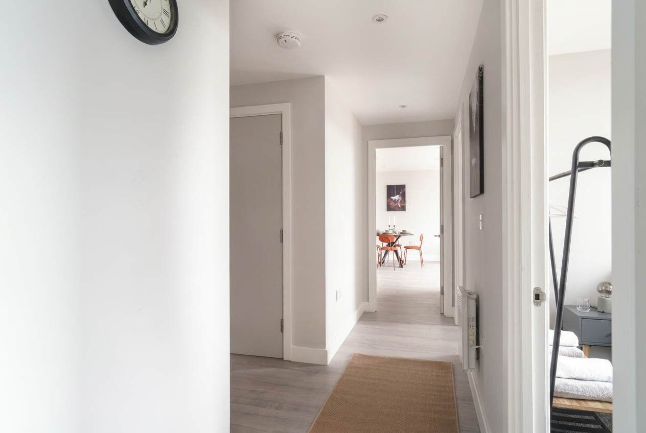 Een gang die uitkomt in een eetruimte met een tafel en stoelen, een klok aan de muur en een radiator op de vloer.