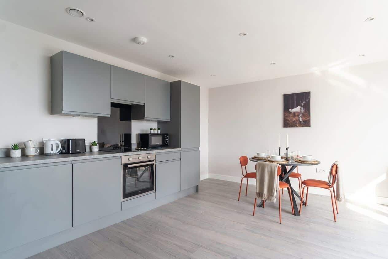 Een moderne keuken met grijze kastjes, een eettafel met stoelen en een schilderij aan de muur.