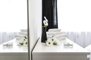 A white bathroom vanity with a mirror, a vase with white flowers, and a stack of white towels.
