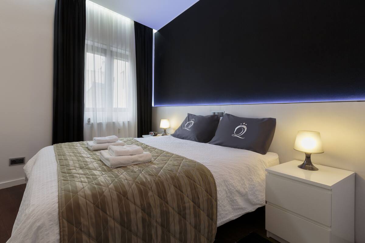 Ein ordentlich bezogenes Bett mit einer gesteppten Decke, einer Nachttischlampe und einem Nachttisch mit Schubladen.
