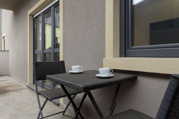 A small outdoor seating area with a table and two chairs, a window, and a door.