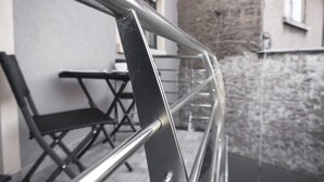 A metal railing with a reflective surface, a black folding chair, and a stone wall in the background.