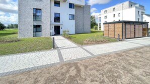 Un edificio moderno de varios pisos con techo plano, ventanas amplias y un área de entrada pavimentada.