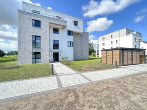 A modern multi-story building with a flat roof, large windows, and a paved entrance area.