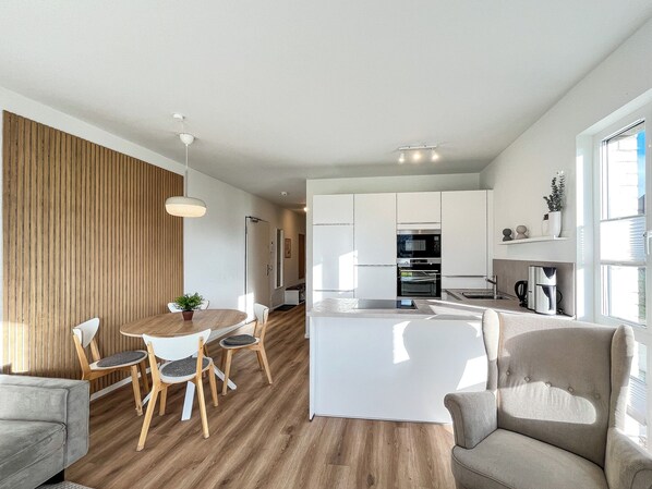A modern kitchen with built-in appliances, a dining area with a round table and chairs, and a cozy seating area with a sofa and armchair. - Weiße Villen Wohnung 12 (Ostseebad Boltenhagen)