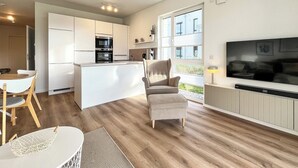 Una cocina moderna con armarios blancos, horno empotrado y zona de comedor con mesa y sillas.
