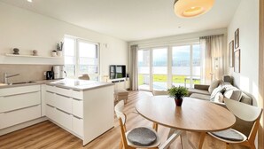Una cocina moderna con una isla central, un comedor con una mesa redonda y sillas, y un amplio ventanal con vistas al exterior.