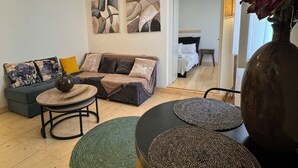 A modern living room with a sofa, coffee table, and ottoman, a large vase with flowers, and abstract wall art. - THE CENTRIC Apt. by LOC HOSPITALITY (Corfu)