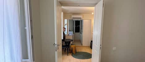 A room with a wooden floor, a bed with a rolled towel, and an open door leading to a dining area with a table and chairs.
