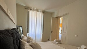 A bedroom with a bed, a dark-colored sofa, a door, and a window with curtains. - THE CENTRIC Apt. by LOC HOSPITALITY (Corfu)