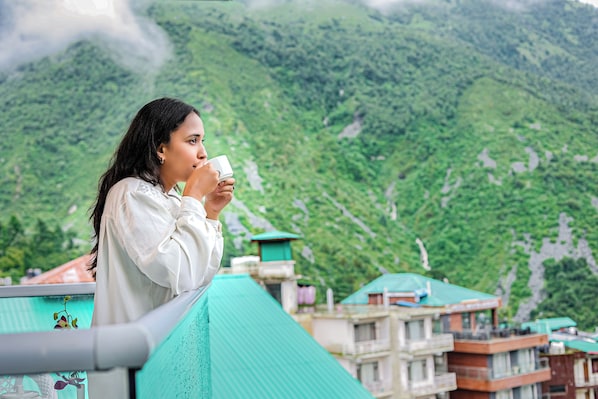 A person standing on a balcony overlooking a mountainous landscape with buildings in the background.