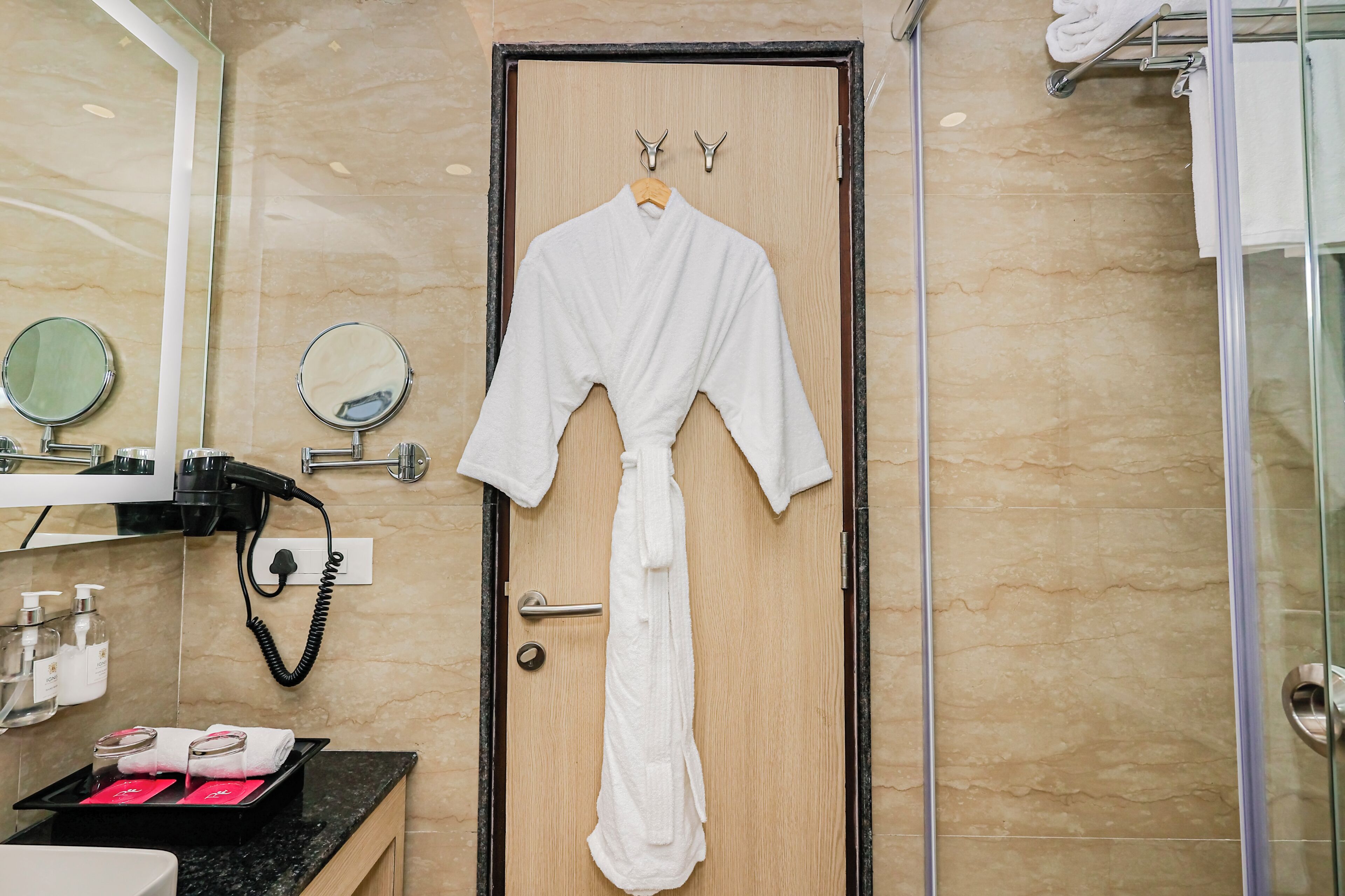 A bathroom with a wooden door, a robe hanging on the door, a mirror, and a towel rack.