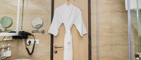 A bathroom with a wooden door, a robe hanging on the door, a mirror, and a towel rack.