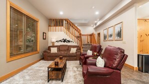 Un salon spacieux avec un escalier, un canapé en cuir marron, un fauteuil en cuir rouge et une table basse en bois.