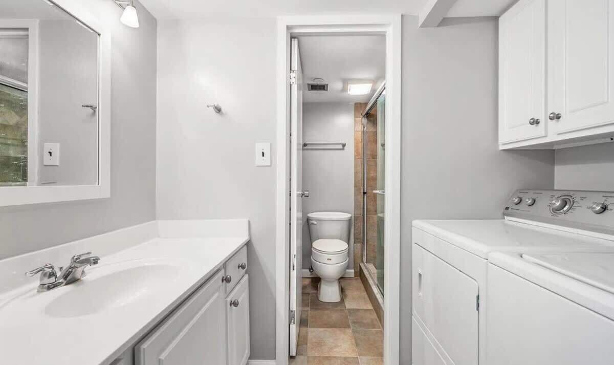 A narrow hallway leading to a bathroom with a toilet, a sink, and a washing machine.