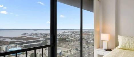 A hotel room with a large window offering a view of a cityscape and a body of water.