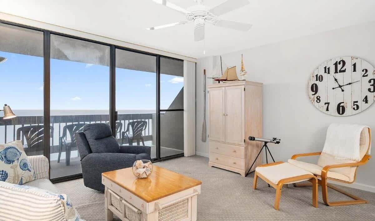 A spacious balcony with a clear view of the ocean, a wooden table, a chair, a clock, and a cabinet.