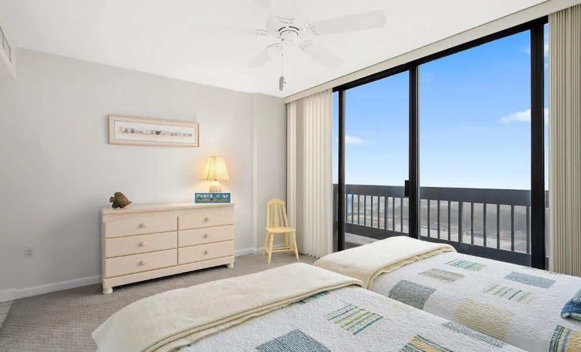 Un dormitorio con dos camas, un aparador, una silla y vistas al balcón.