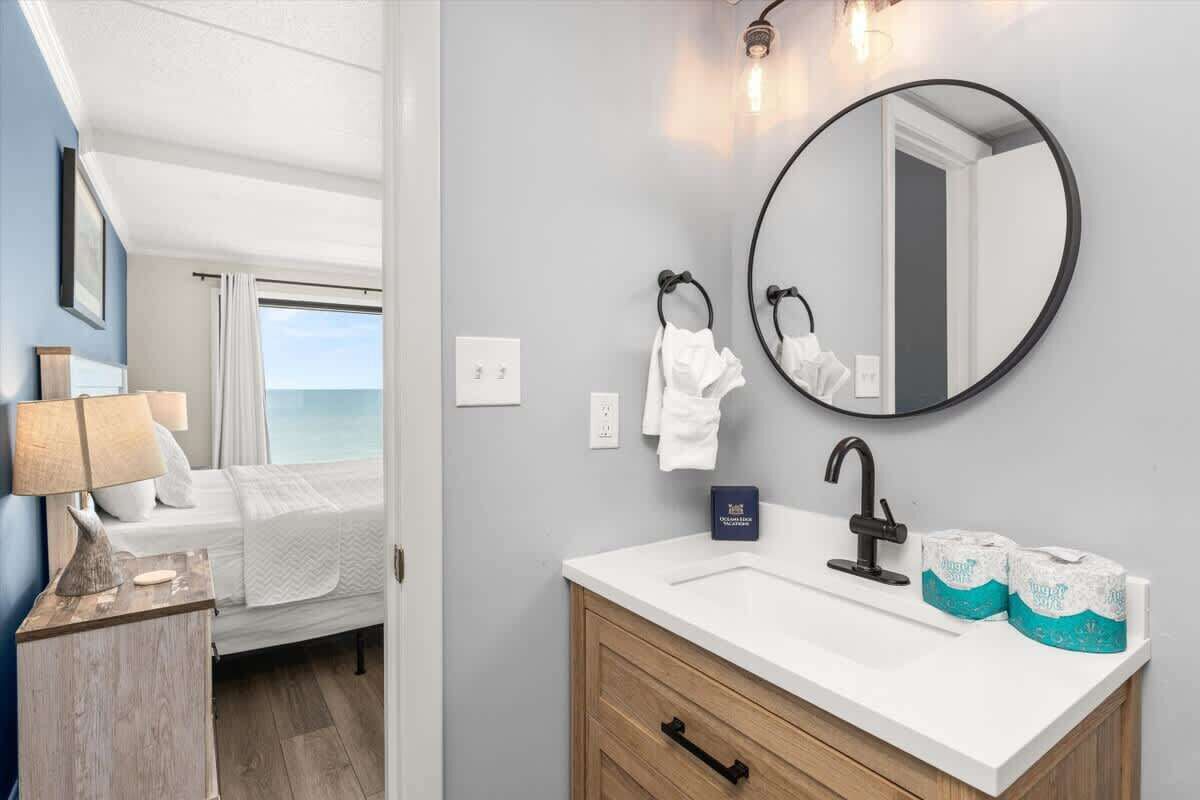 Un baño con un lavabo blanco, un espejo redondo y dos rollos de papel higiénico.