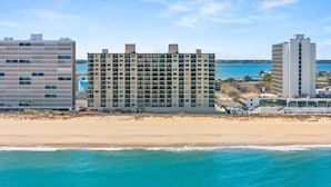 Ein Strandhotel mit mehreren Etagen, ein sandiger Strand im Vordergrund und freie Sicht auf das Meer.