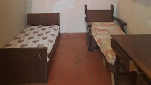 Een kleine, schemerige kamer met twee houten bedden, een tafeltje en een plank aan de muur.