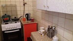 Een keuken met een gasfornuis, een waterkoker en een tafel met mokken en bestek.
