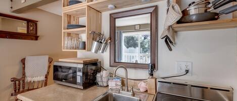 A kitchen with a built-in microwave, stainless steel sink, wooden shelves, and a window with a view.