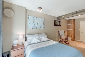 A bedroom with a bed, bedside table, fan, lamp, and a rocking chair.