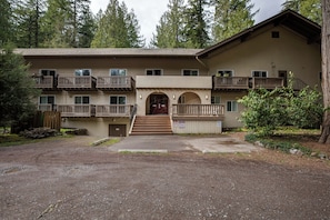 A multi-story building with balconies, a central entrance, and a surrounding natural landscape.