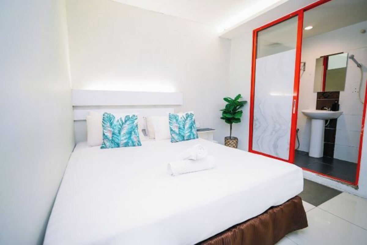A modern hotel room with a large bed, white bedding, and a red-framed sliding door leading to a bathroom.