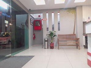 A reception area with a bench, a potted plant, a fire extinguisher, and a glass door.