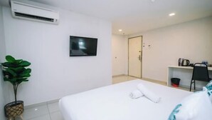Una camera d'albergo con un letto, una televisione, una scrivania e una pianta.