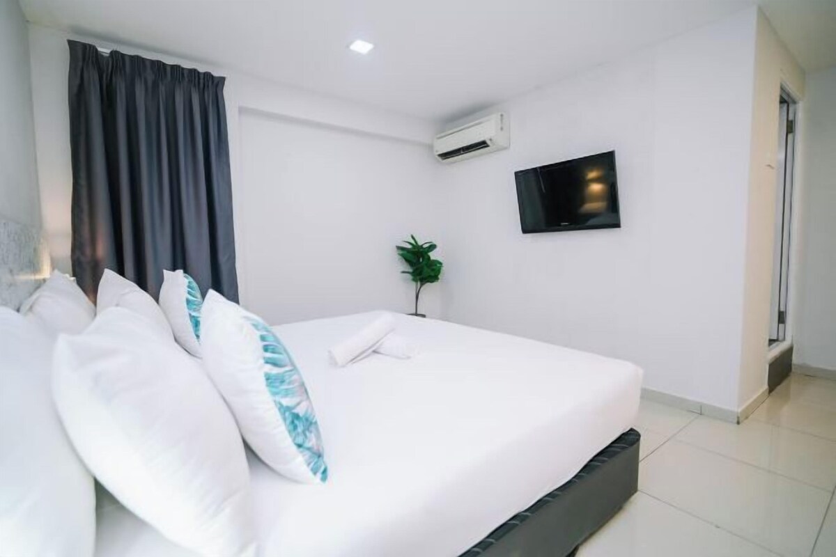 A modern hotel room with a large bed, white bedding, a flat-screen TV mounted on the wall, and an air conditioning unit.