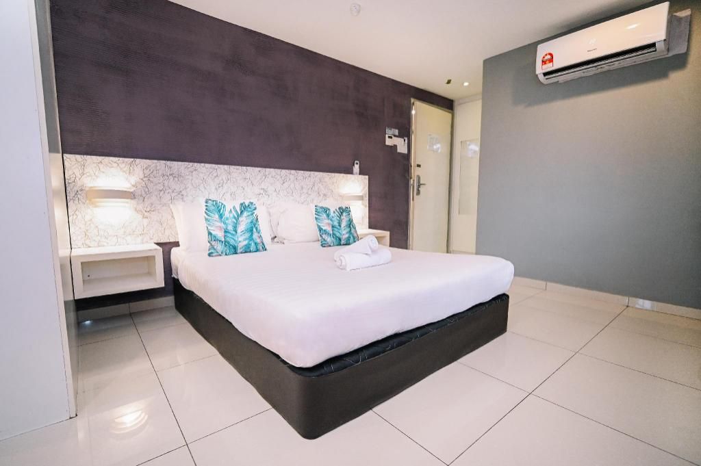 A modern hotel room with a large bed, bedside tables, a marble headboard, and an air conditioning unit.