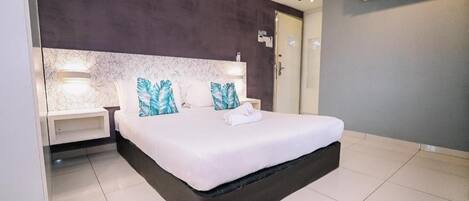 A modern hotel room with a large bed, bedside tables, a marble headboard, and an air conditioning unit.