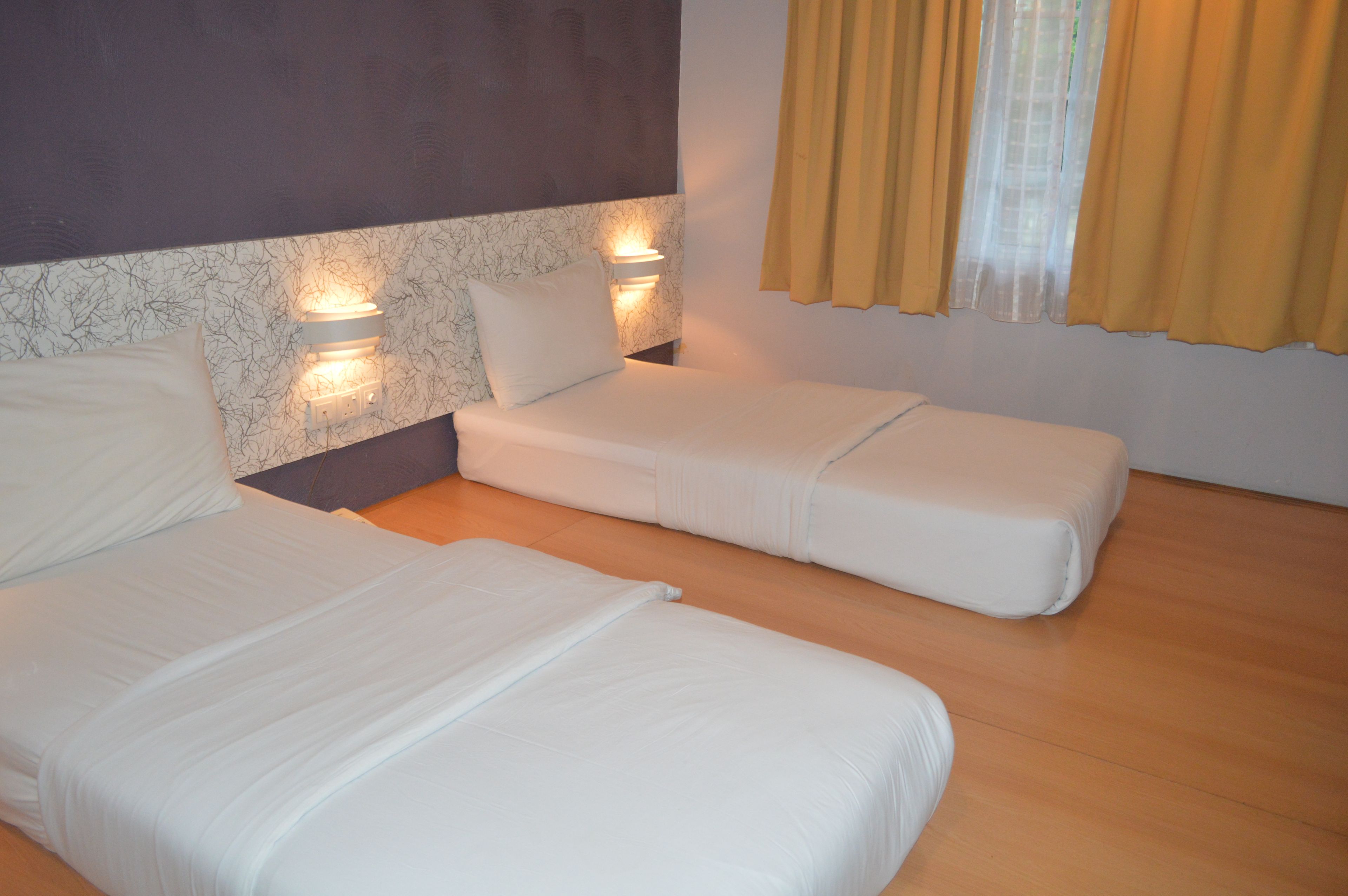 A hotel room with two beds, a marble-patterned wall, and a window with yellow curtains.