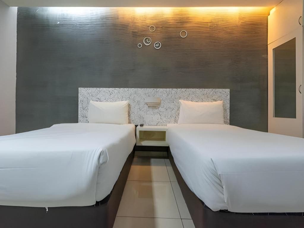 A hotel room with two beds, a marble headboard, and a wall-mounted light fixture.