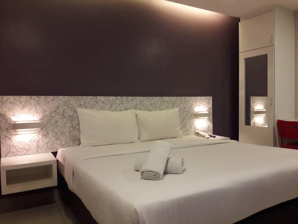 Una habitación de hotel con cama, mesitas de noche, teléfono y armario.