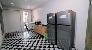 A kitchenette with two black refrigerators, a wooden cabinet, a chair, and a checkered floor. - Swing & Pillows @ PJ SS2 (Petaling Jaya)