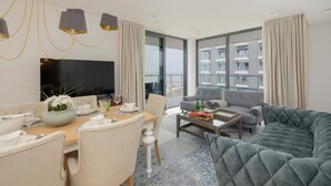 Una sala moderna con comedor, un sofá gris, un televisor de pantalla plana y grandes ventanales con vista a la ciudad.