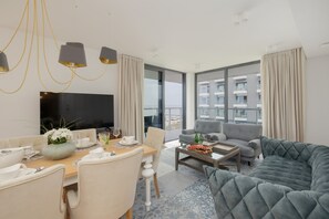 Un salon moderne comprenant un coin repas, un canapé gris, un téléviseur à écran plat et de grandes fenêtres donnant sur la ville.