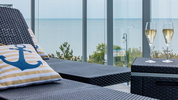 Un balcón con vista al mar, dos copas de champán y un cojín a rayas con diseño de ancla.