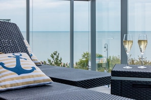 Balkon med udsigt over havet, to glas champagne og en stribet pude med anker-motiv.