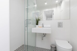 A modern bathroom with a glass-enclosed shower, a white sink, and a toilet.