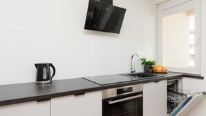 A modern kitchen with a black countertop, stainless steel appliances, a black range hood, and a window with a view.