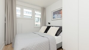 A modern bedroom with a bed, a window with curtains, a radiator, and a framed picture on the wall.