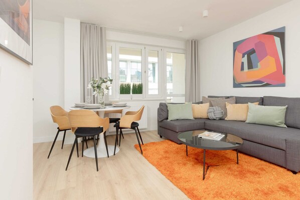 A modern living room with a grey sofa, orange rug, and a dining area with chairs and a table.