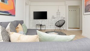 A modern living room with a grey sofa, a black chair, a small round table, and a flat-screen TV mounted on the wall.