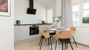 A modern kitchen with white cabinets, a black range hood, and a dining area with a round table and four chairs.