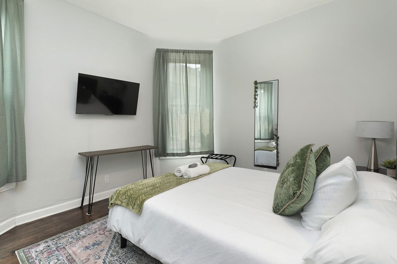 A modern bedroom with a bed, a desk, a TV, and a mirror.